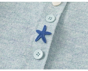 Detail van lichtblauw gebreid vest met witte hartjesknoop en marineblauwe zeester borduursel