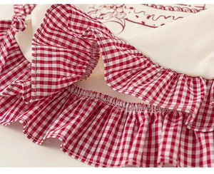 Detail of girls' cream ribbed fabric top featuring red gingham ruffled trim and stitching