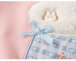 Detail van roze sweatshirt met schattige konijnenpatch, blauw ruitje en een zacht strikje