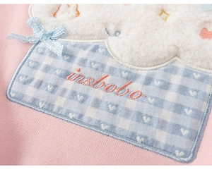 Detail van roze sweatshirt met wolkenapplicatie, blauwe ruitjes en strikborduursel