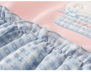 Detail van een roze katoenen sweatshirt met blauw geblokte ruches en geborduurde strikpatch