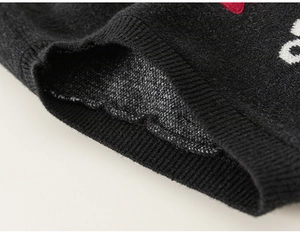 Close-up detail of black knit fabric with red heart embroidery and ribbed cuff texture