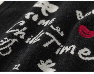 Detail of black knit cardigan featuring white jacquard text and a red heart smile patch