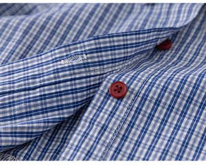 Macro shot of blue gingham fabric with a contrasting dark red four-hole button and stitching