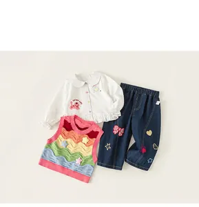 Detail of girls' white shirt with embroidery, rainbow knit vest, and bow jeans set
