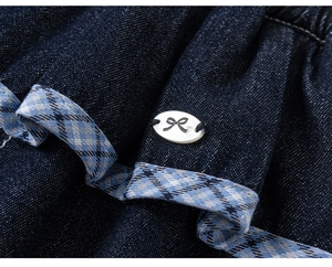 Close-up of dark blue denim fabric with plaid piping and white bow decorative button