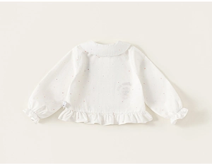 Macro shot of white baby sweater featuring colorful polka dots and ruffled hem texture