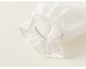 Detailed close-up of elastic ruffled cuffs on a soft white cotton sweater with colorful polka dots