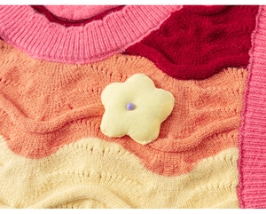 Close-up of knit vest featuring colorful wave patterns and a 3D yellow flower detail