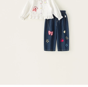 Detail von weißem Baumwollhemd mit Katzenstickerei und Denim-Hose mit bunten Aufnähern