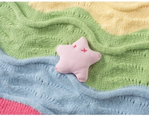 Close-up of a plush pink star charm with cross-stitched eyes on a colorful knit background