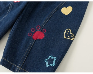 Detailed close-up of dark blue denim jeans with cute colorful embroidery and golden stitching