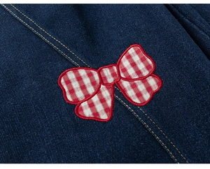 Detail of denim fabric with golden stitching and a red gingham bow embroidery patch