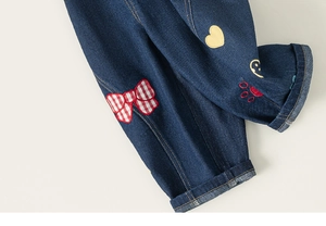 Dettaglio di jeans blu scuro con fiocchi rossi ricamati e motivi a cuore stile cartone
