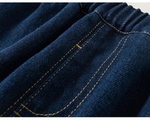 Dettaglio macro dei jeans in denim blu scuro con elastico in vita e cuciture arancioni