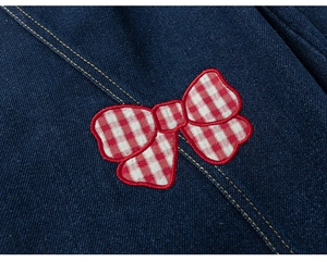 Dettaglio del fiocco a quadretti bianchi e rossi su jeans bimba blu scuro con cuciture gialle