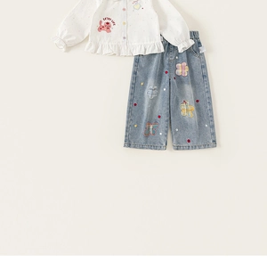Dettaglio camicia bianca con volant e gatto e jeans con ricami floreali colorati