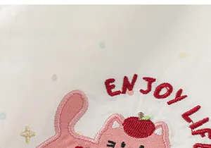 Dettaglio di ricamo gatto rosa e scritta Enjoy Life su camicia a pois bianchi