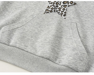 Detail des grauen Hoodies mit Kängurutasche und Stern-Aufnäher im Leopardenmuster-Stil