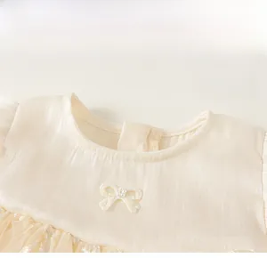 Detail of champagne girls dress featuring a round neckline and pearl bow accent