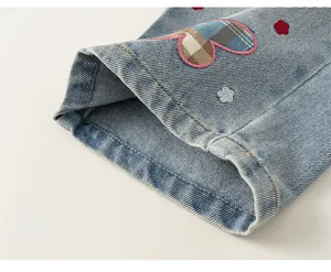 Dettaglio dell'orlo dei jeans da bambina con toppa a cuore e ricami floreali
