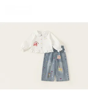 Dettaglio di camicia bianca per bambina con ricamo gatto e pantaloni denim con fiori