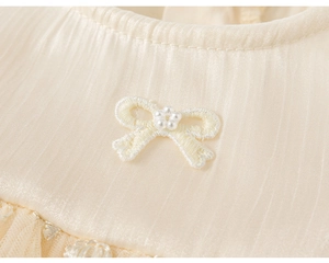 Detail of girl's dress featuring pleated cream fabric with pearl-studded bow embroidery