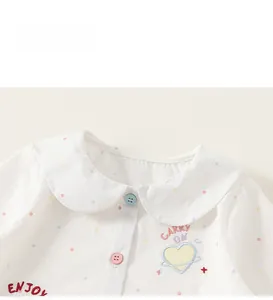 Dettaglio camicia in cotone bianco con pois colorati, colletto Peter Pan e ricamo arcobaleno