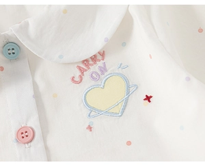 Dettaglio camicia da bambina in cotone bianco a pois con colletto a bambola e ricamo
