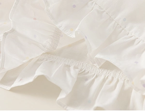 Dettaglio del tessuto bianco a pois colorati con balze e cuciture di alta qualità