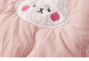 Close-up of pink quilted fabric featuring a white sheep plush patch with embroidery