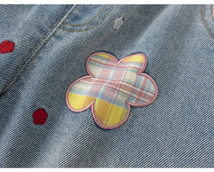 Dettaglio del tessuto denim blu chiaro con toppe floreali a quadri arcobaleno e ricami