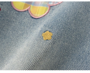 Dettagli del tessuto denim blu chiaro con ricamo floreale dorato e inserto patchwork a quadretti