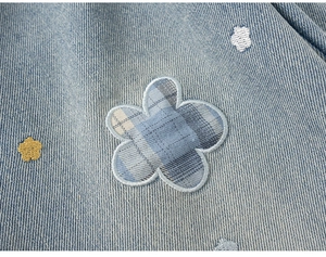 Dettaglio del ricamo floreale e della trama denim sui jeans azzurri da bambina