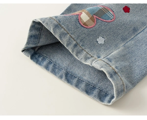 Dettaglio di jeans per bambina con toppa a cuore a quadri e ricami floreali