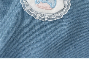 Close-up of blue denim fabric with floral embroidery and white lace ruffle detail
