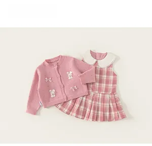 Flachbild-Detail von rosa Strickjacke mit Schleife und kariertem Kleid für Mädchen