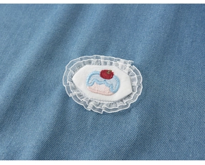 Close-up of cupcake embroidery and lace detail on a blue denim girl dress