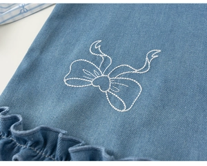 Detail of blue denim dress with white bow embroidery and ruffled hem for girls