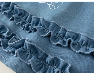 Detailed macro view of denim dress featuring ruffled edges and white embroidered bows