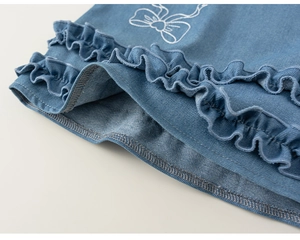 Detail of light blue denim dress hem with white bow embroidery and double ruffle trim