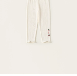 Détail de leggings blancs côtelés avec broderie cerise et ourlet à volants fille