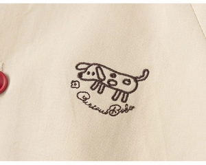 Detail of Curious Bobo puppy embroidery on beige cotton jacket with a red button