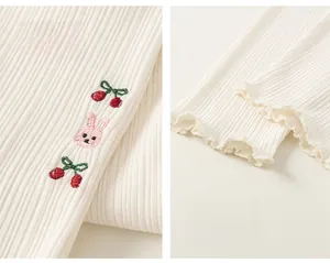 Détail du tricot blanc côtelé avec broderie cerise lapin et bords volantés aux chevilles