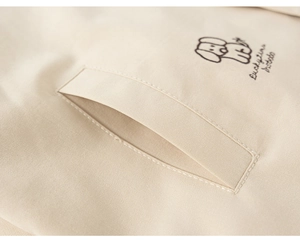 Detail of light beige boy's jacket with cute cartoon dog embroidery and slit pocket