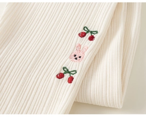 Gros plan sur le tricot côtelé beige avec des détails brodés de cerises et de lapins