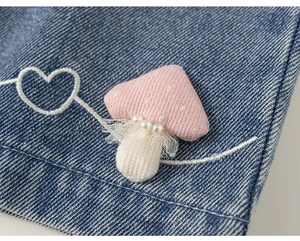 Dettaglio della toppa in maglia a fungo rosa con pizzo e perle su tessuto denim