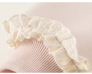 Dettaglio di maglia a coste rosa con bordo in pizzo floreale bianco e ricamo fine