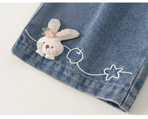 Dettaglio del ricamo con coniglietto di peluche e motivi a stelle su jeans per bambini