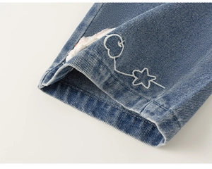 Dettaglio del risvolto dei jeans blu con ricami di stelle e mele sulla stoffa